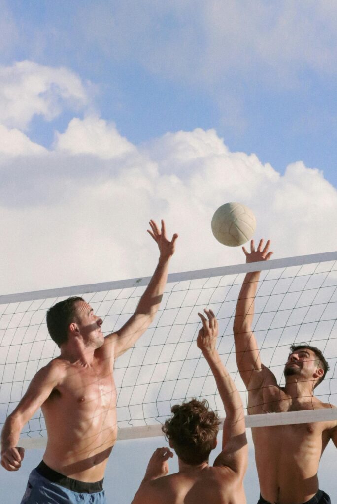Men playing beach volleyball against a cloudy sky, showcasing athleticism and teamwork.